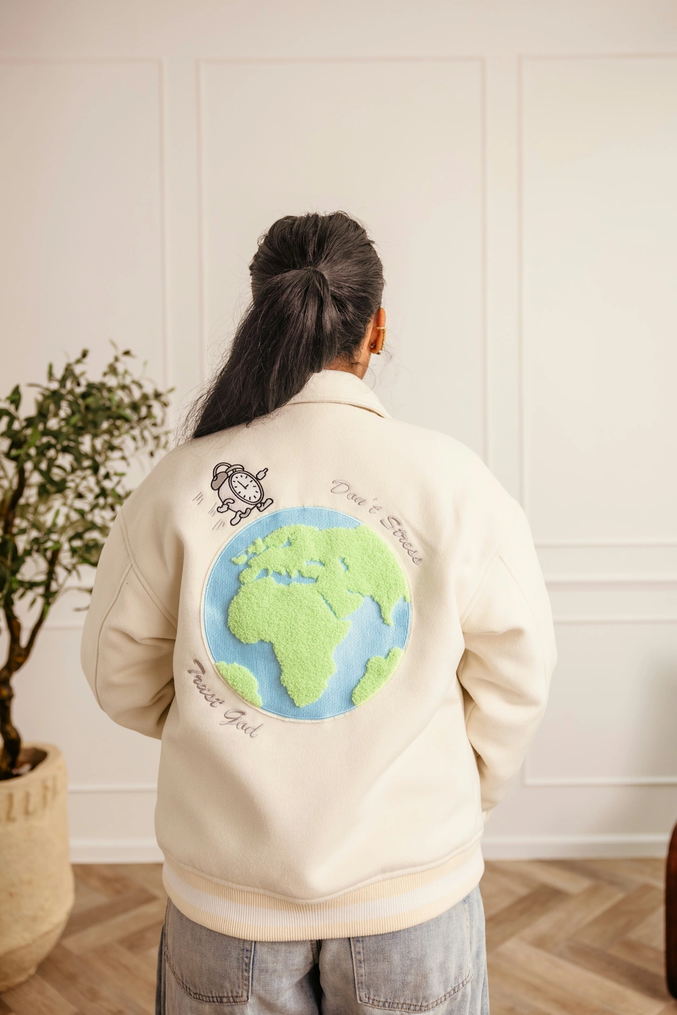 Beige Globe Varsity Jacket — female model, back view showing globe embroidery