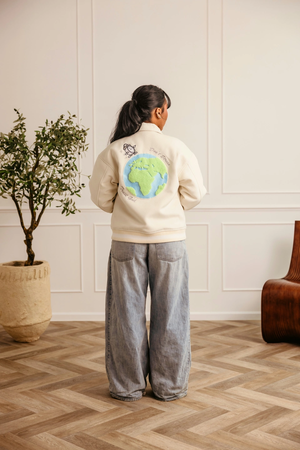 Beige Globe Varsity Jacket — female model, full-length back view showing globe embroidery