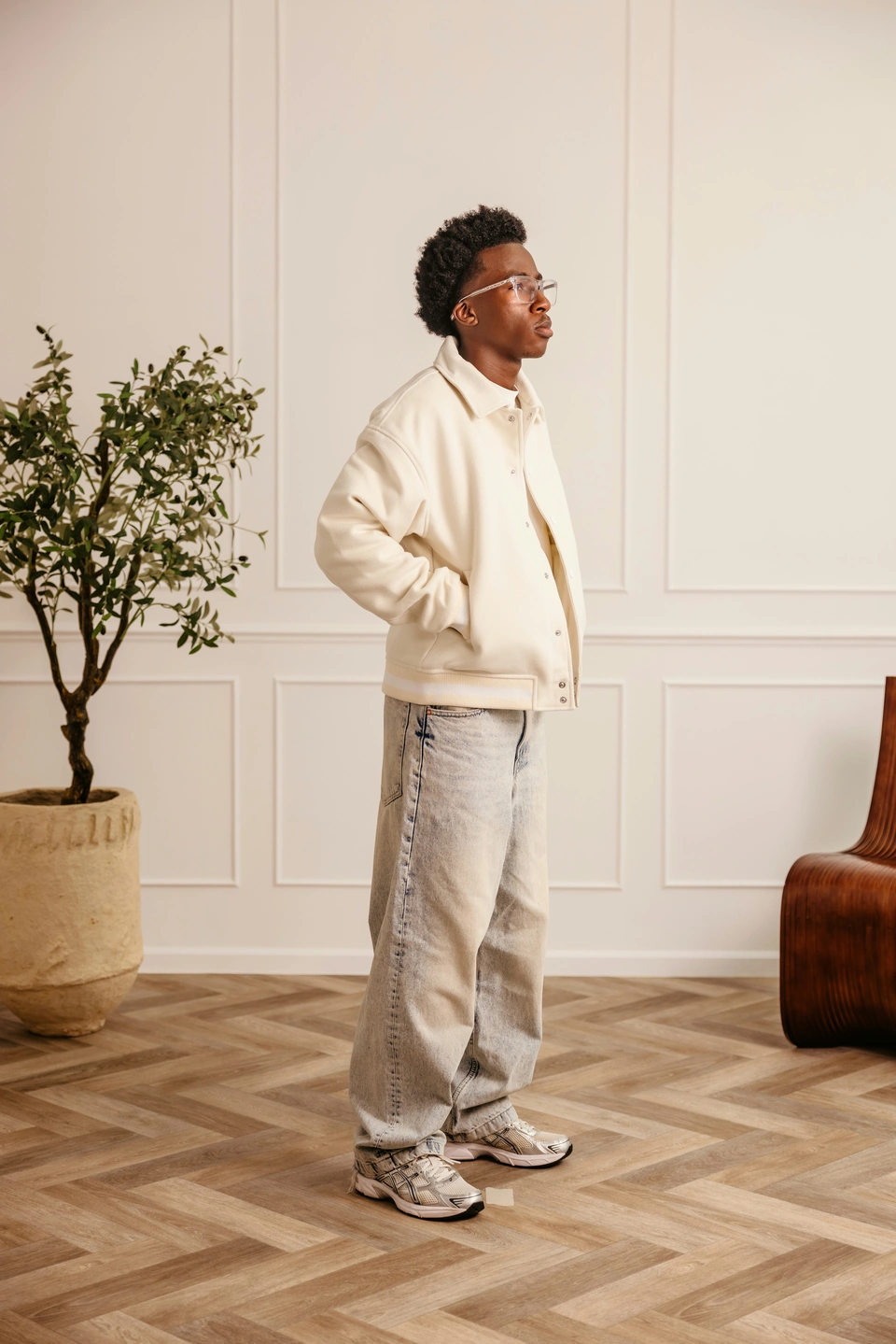 Beige Globe Varsity Jacket — male model, full-length side view with hands in pockets
